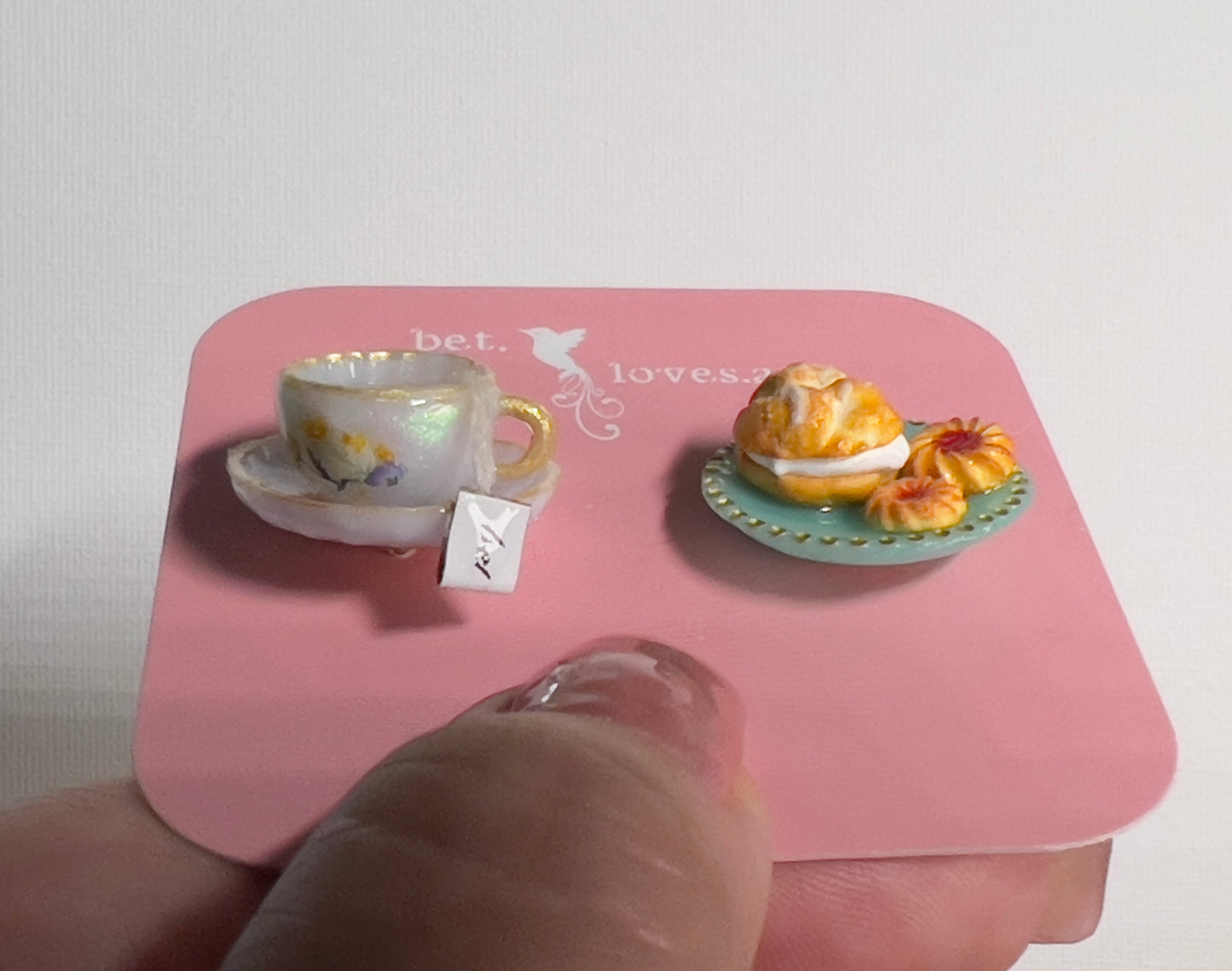 001 - Mini white teacup with tea bag, cream puff and two cookies on teal saucer