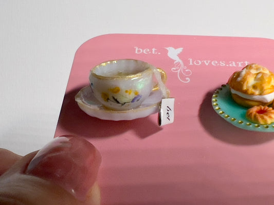 001 - Mini white teacup with tea bag, cream puff and two cookies on teal saucer