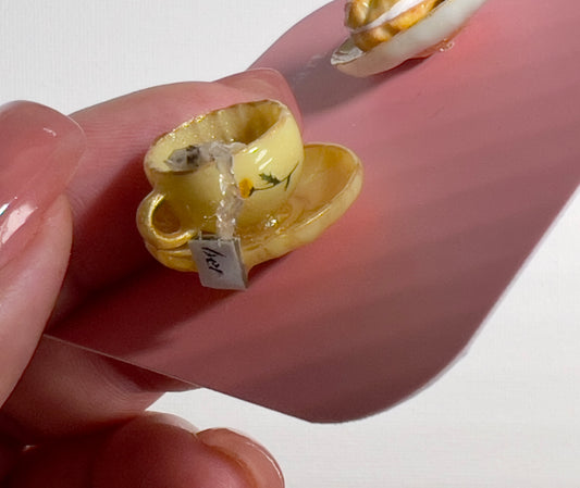 003 - Mini yellow teacup with tea bag, cream puff and chocolates on white saucer